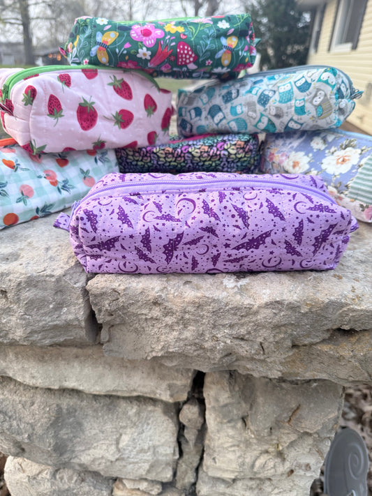 Collection of quilted boxy pouches in assorted fabrics on a stone wall